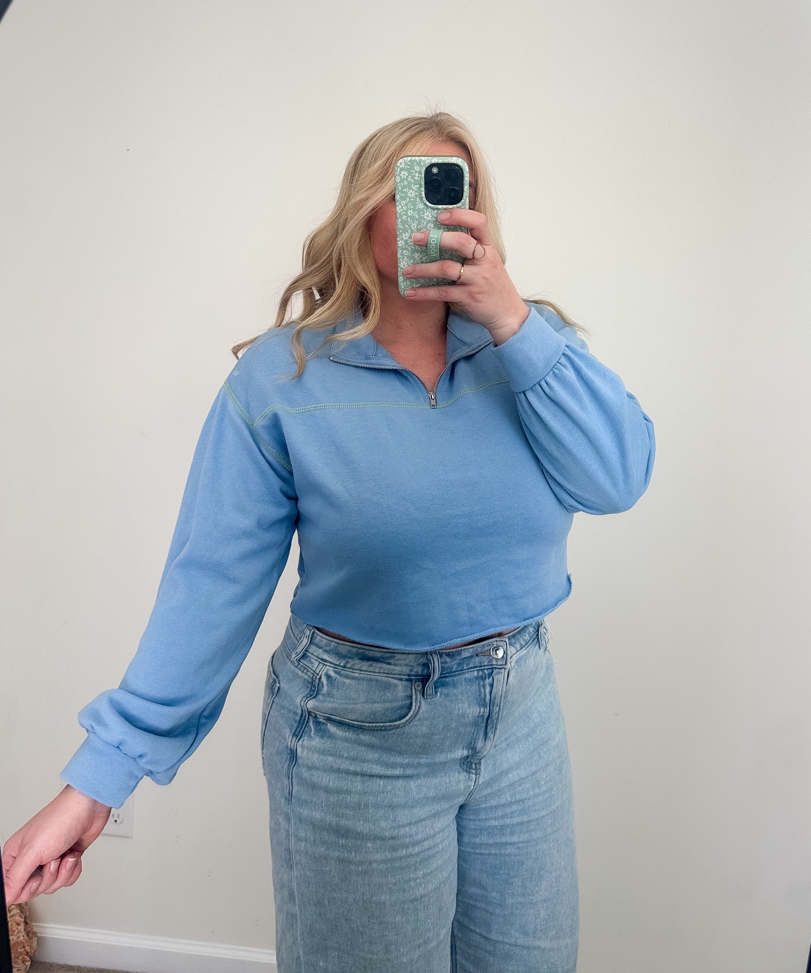 Person wearing a blue long-sleeve top and jeans taking a mirror selfie.