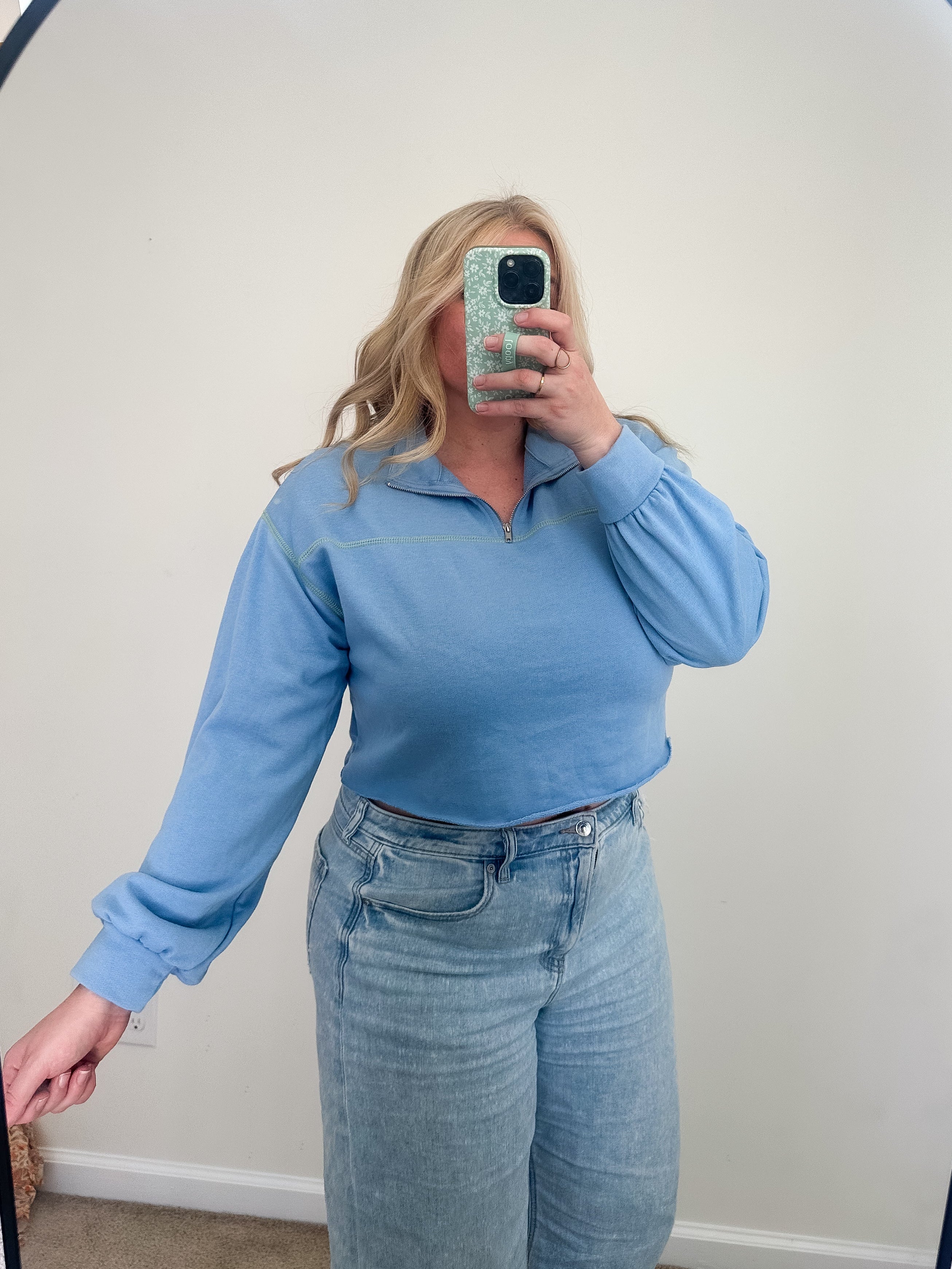 Person wearing a blue long-sleeve top and jeans taking a mirror selfie.