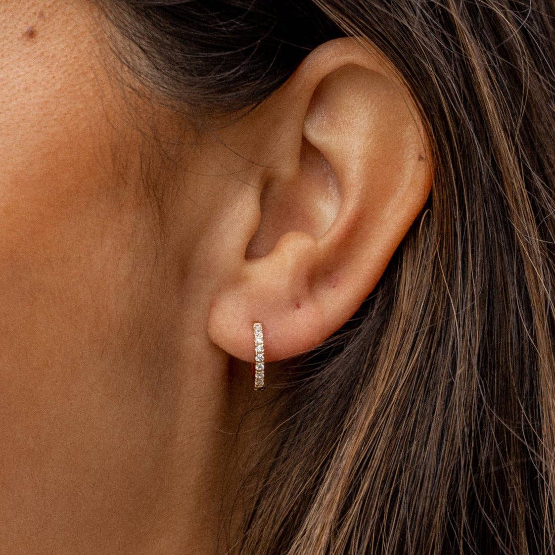 Close-up of an ear wearing a diamond hoop earring with hair partially covering the frame.