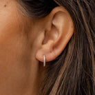 Close-up of an ear wearing a diamond hoop earring with hair partially covering the frame.