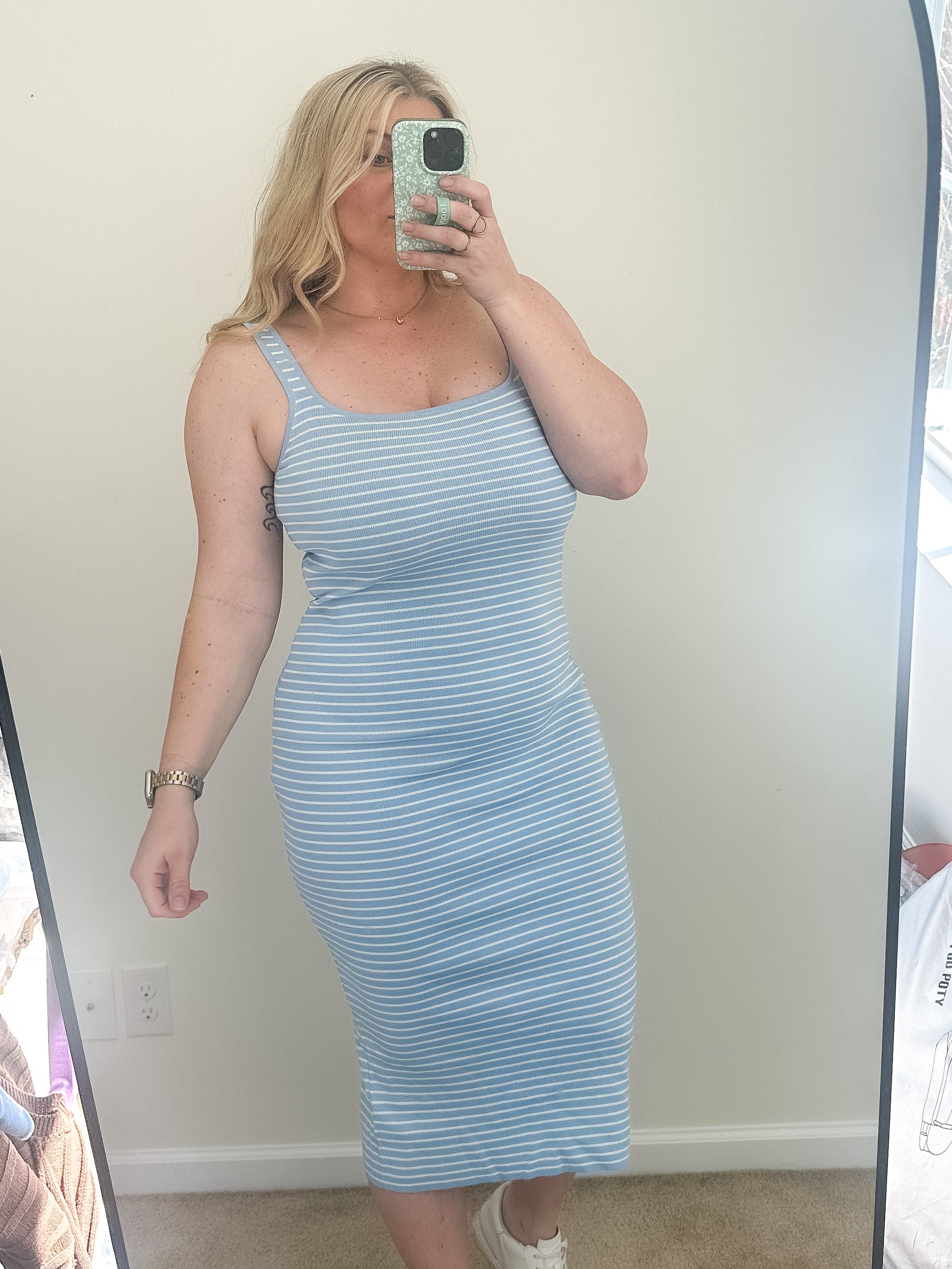 A woman wearing a blue and white striped bodycon midi dress with a deep scoop neckline and spaghetti straps.