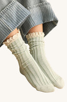 Person wearing green ribbed socks with lace trim on a stone floor.