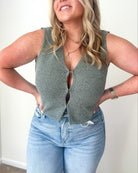 A sleeveless olive green knit vest cardigan with a deep V-neckline and hook-and-eye closure.