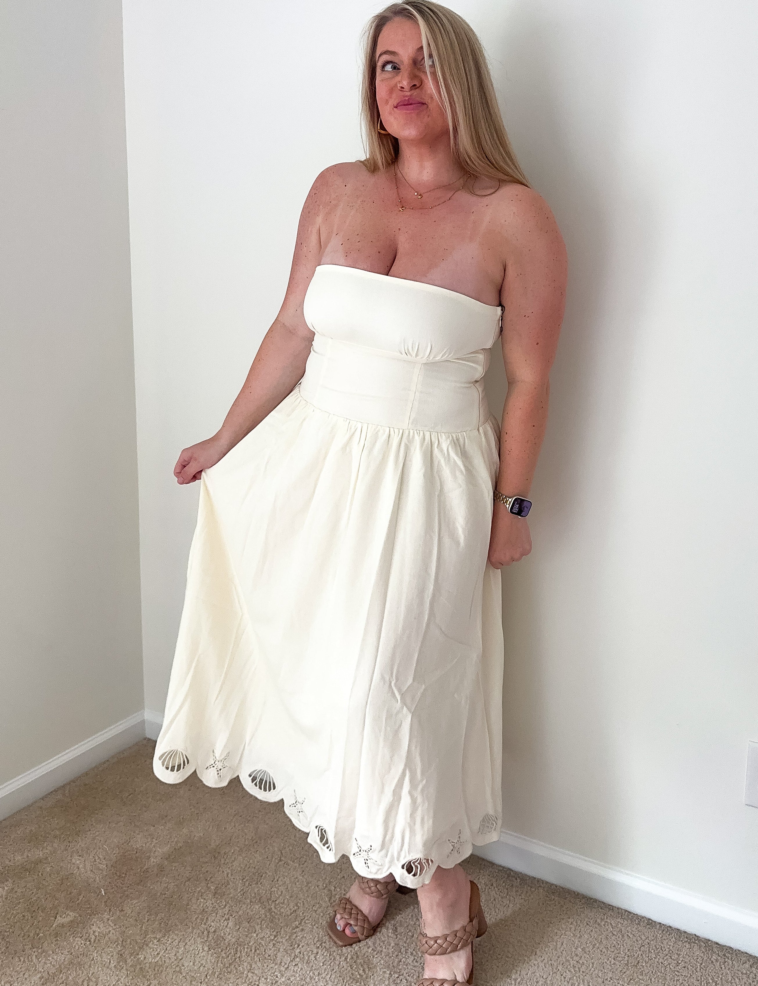 Woman wearing a white strapless dress standing against a plain wall.