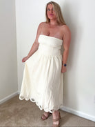 Woman wearing a white strapless dress standing against a plain wall.