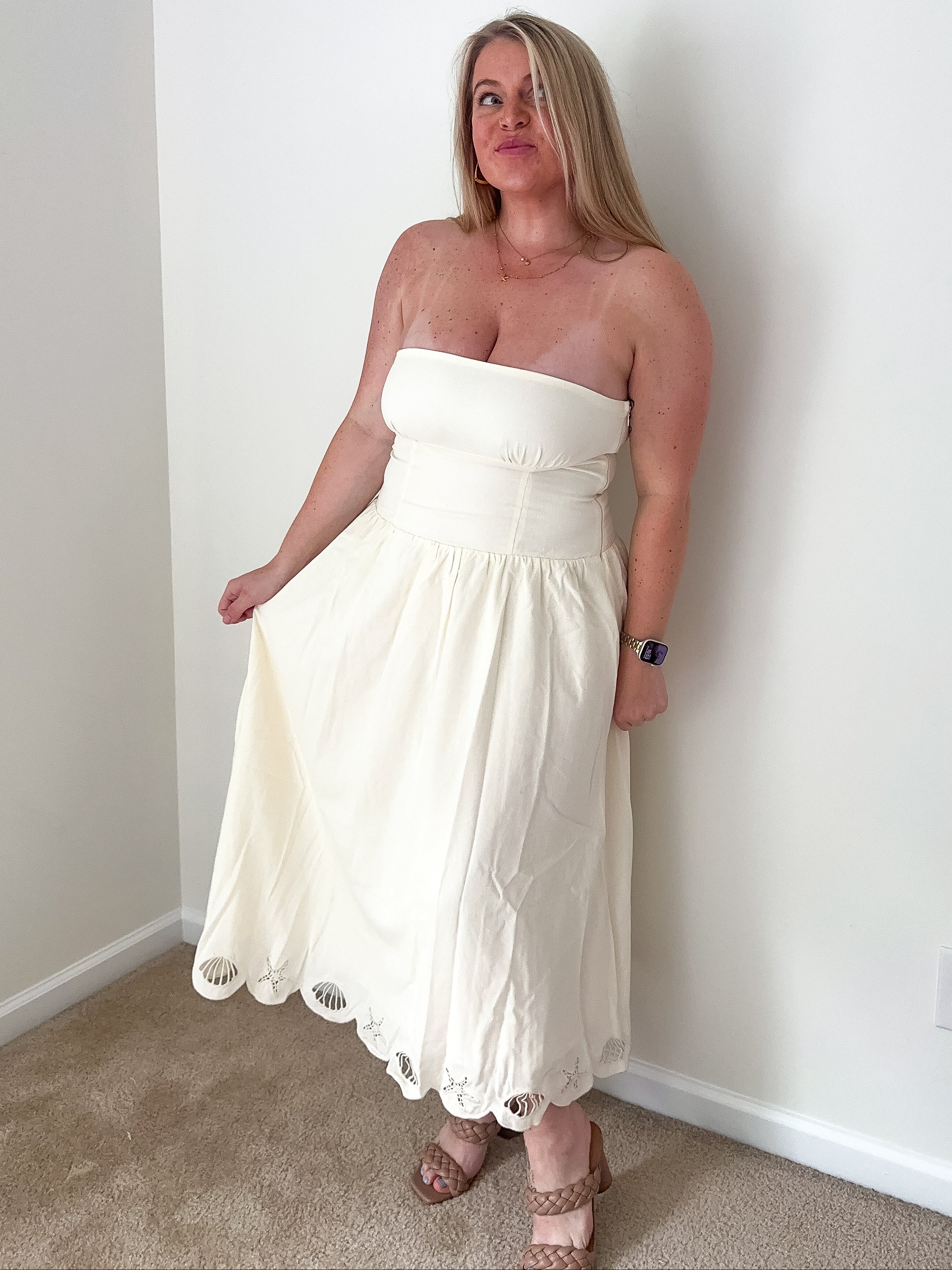 Woman wearing a white strapless dress standing against a plain wall.
