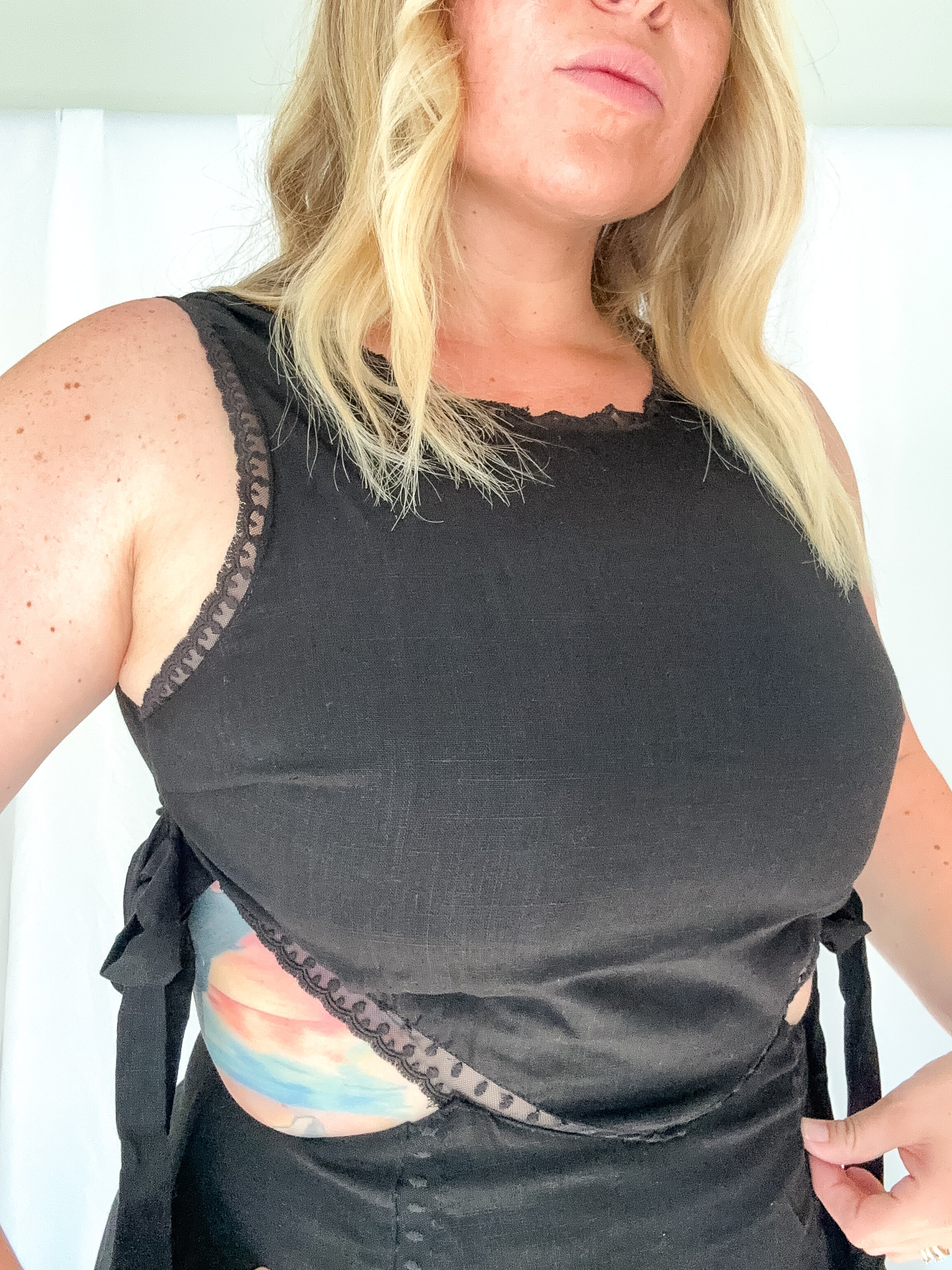 Woman wearing a black sleeveless top with lace trim on a white background