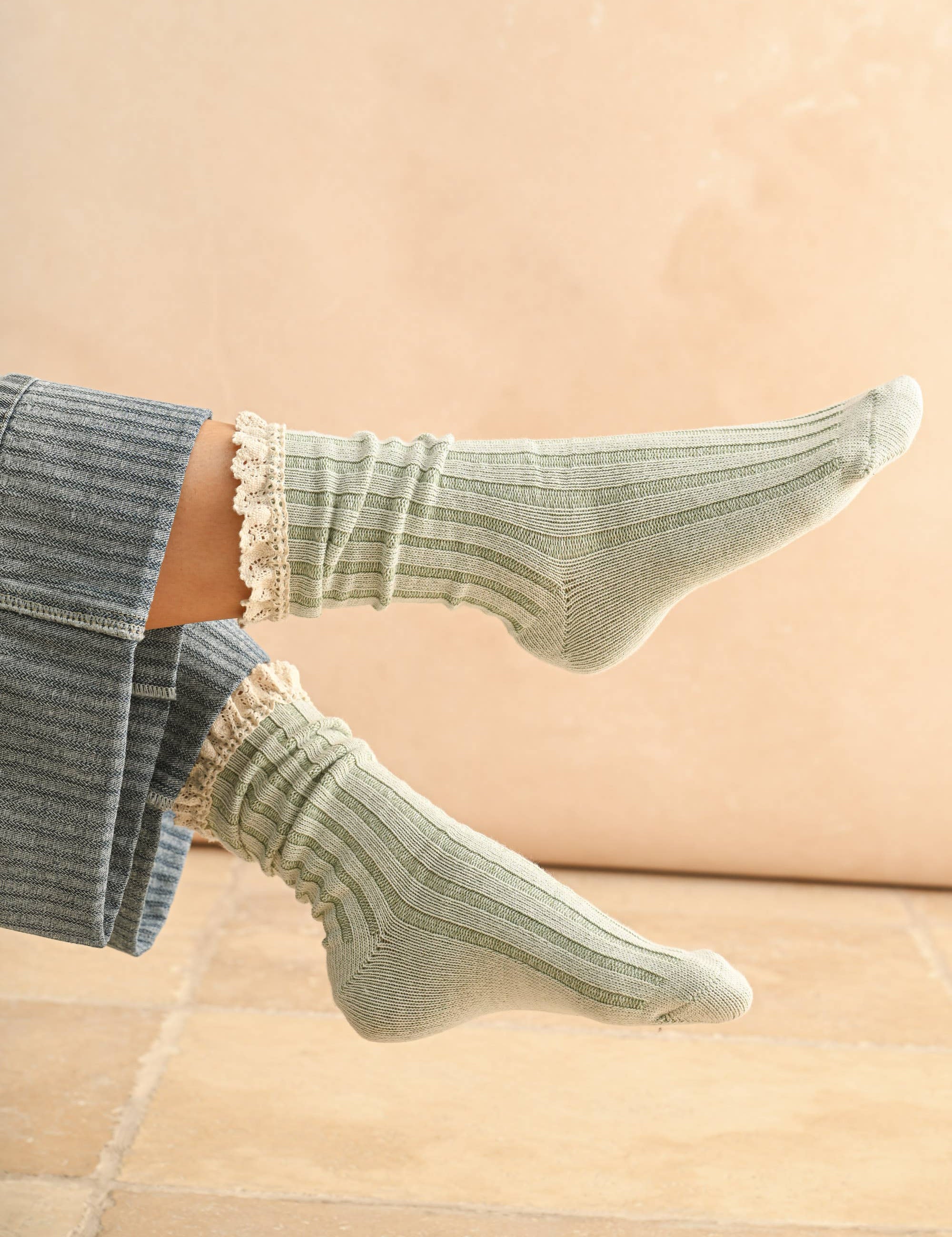 Green socks with ruffled top worn by a person on a beige background