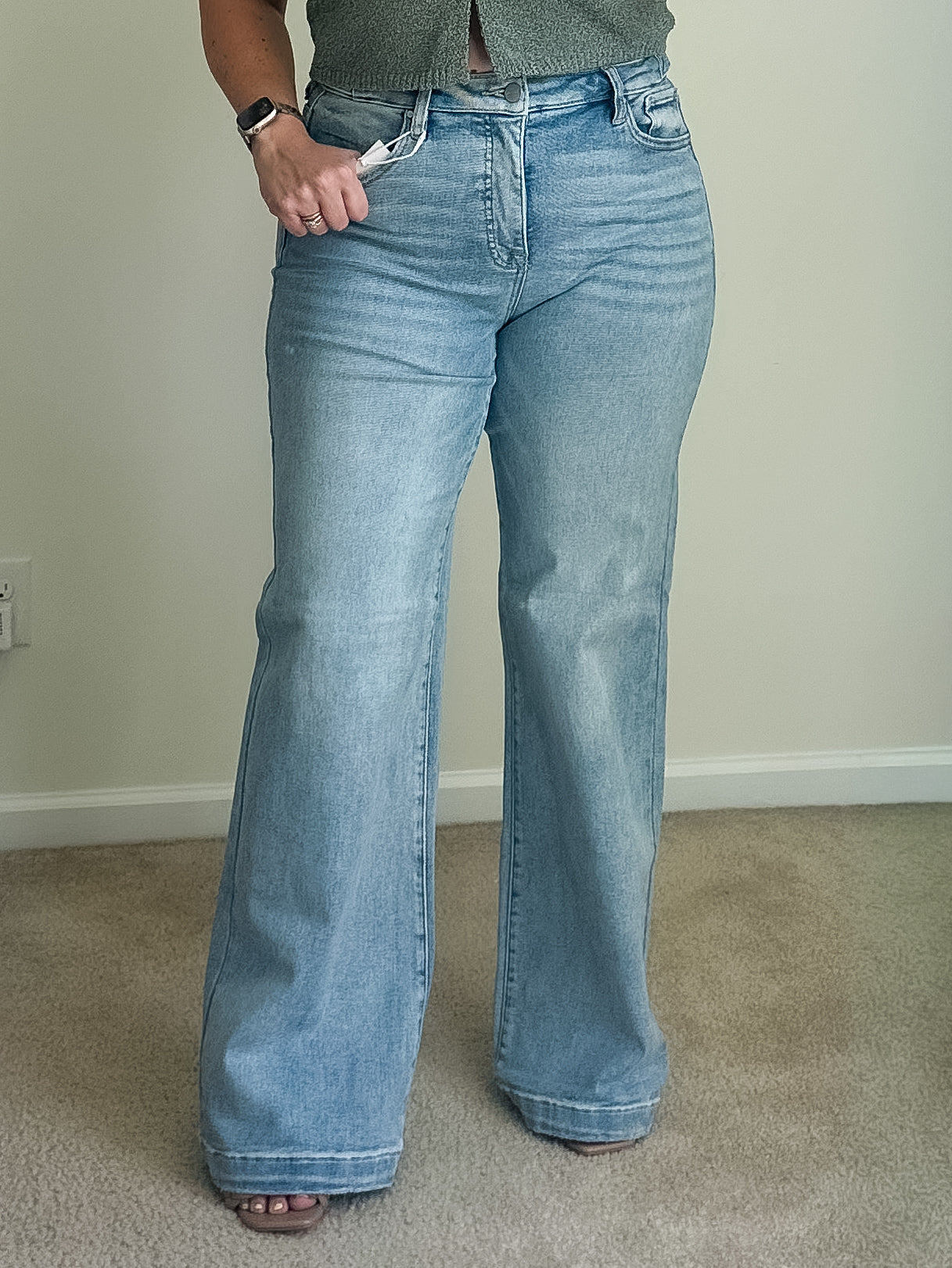 High-rise wide-leg jeans in light wash denim with a button and zip fly, shown worn on a person standing on carpet.