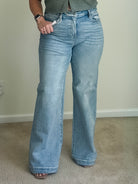 High-rise wide-leg jeans in light wash denim with a button and zip fly, shown worn on a person standing on carpet.