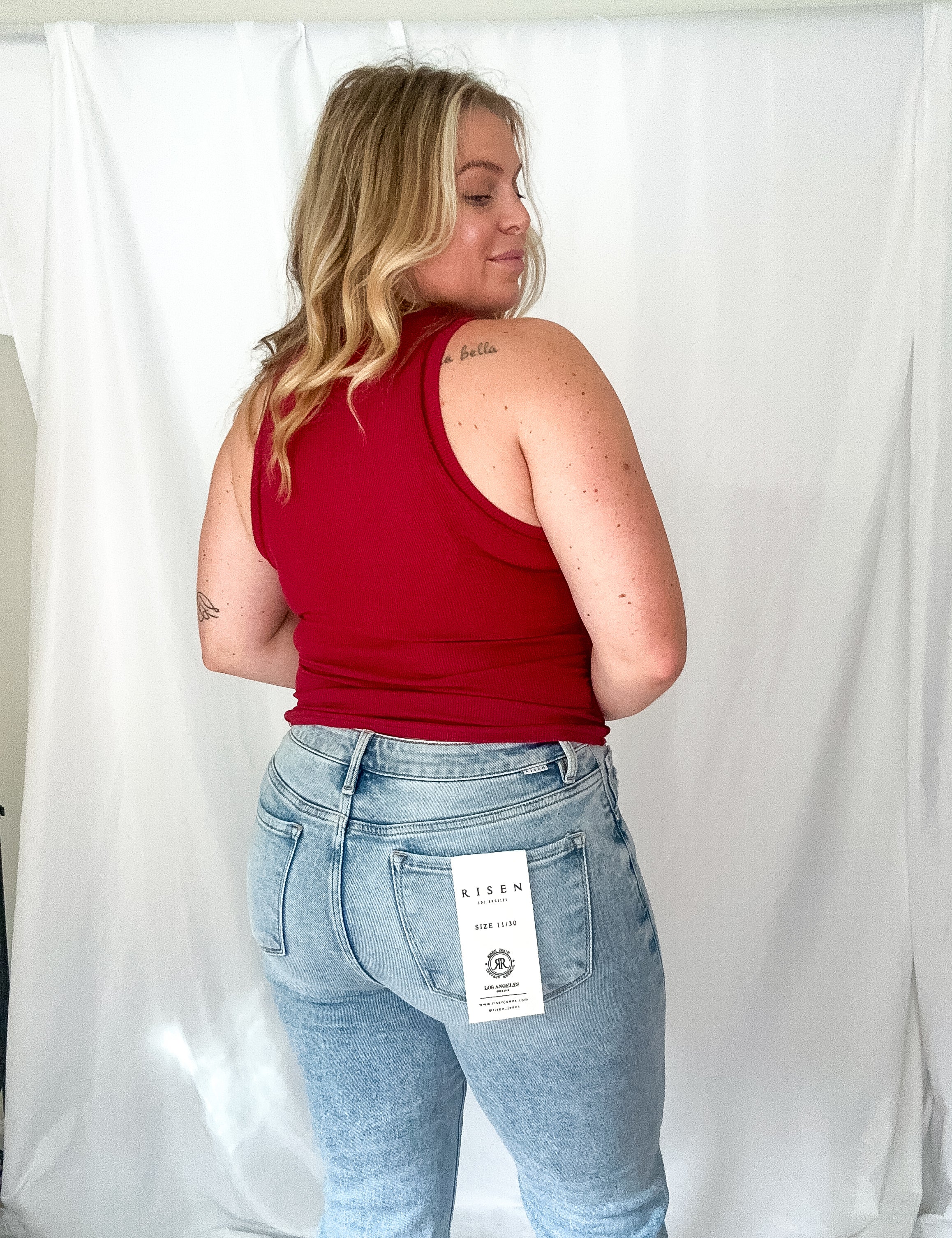 Person wearing a red tank top and light blue jeans with a visible brand tag against a white background