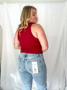 Person wearing a red tank top and light blue jeans with a visible brand tag against a white background