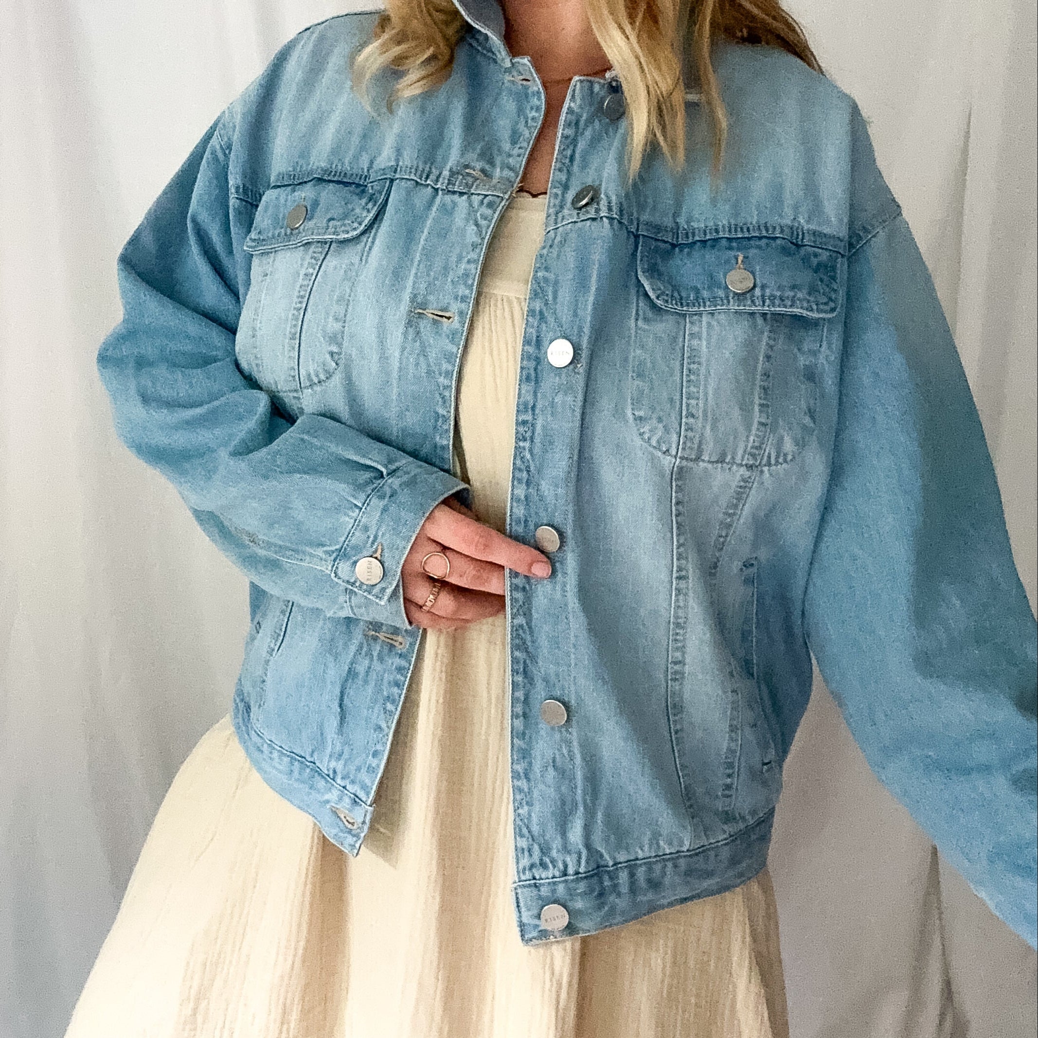 Woman wearing a light blue denim jacket over a beige dress against a white background