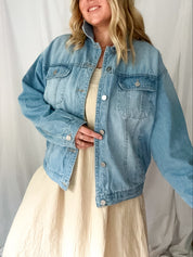 Woman wearing a light blue denim jacket over a beige dress against a white background