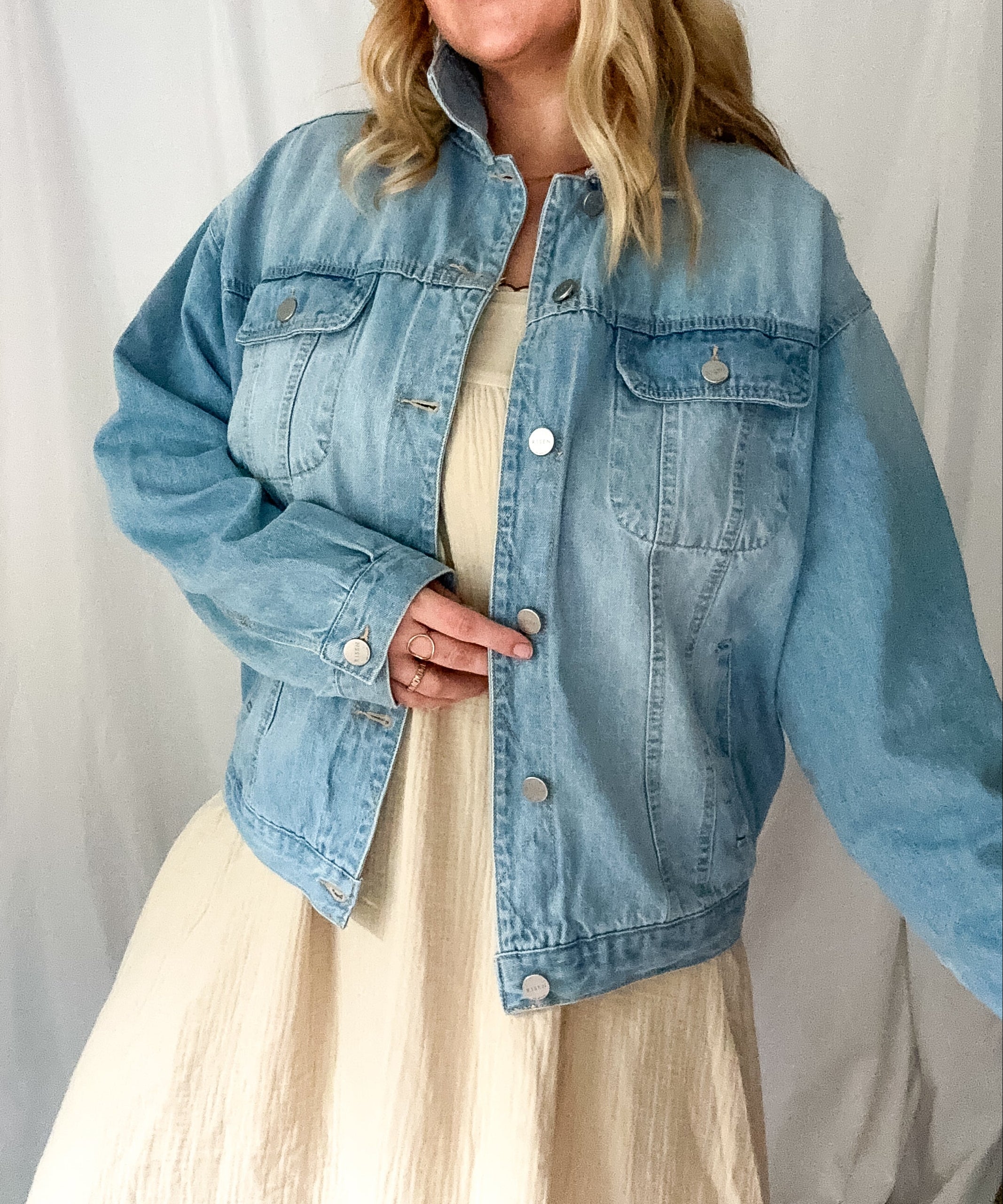 Woman wearing a light blue denim jacket over a beige dress against a white background