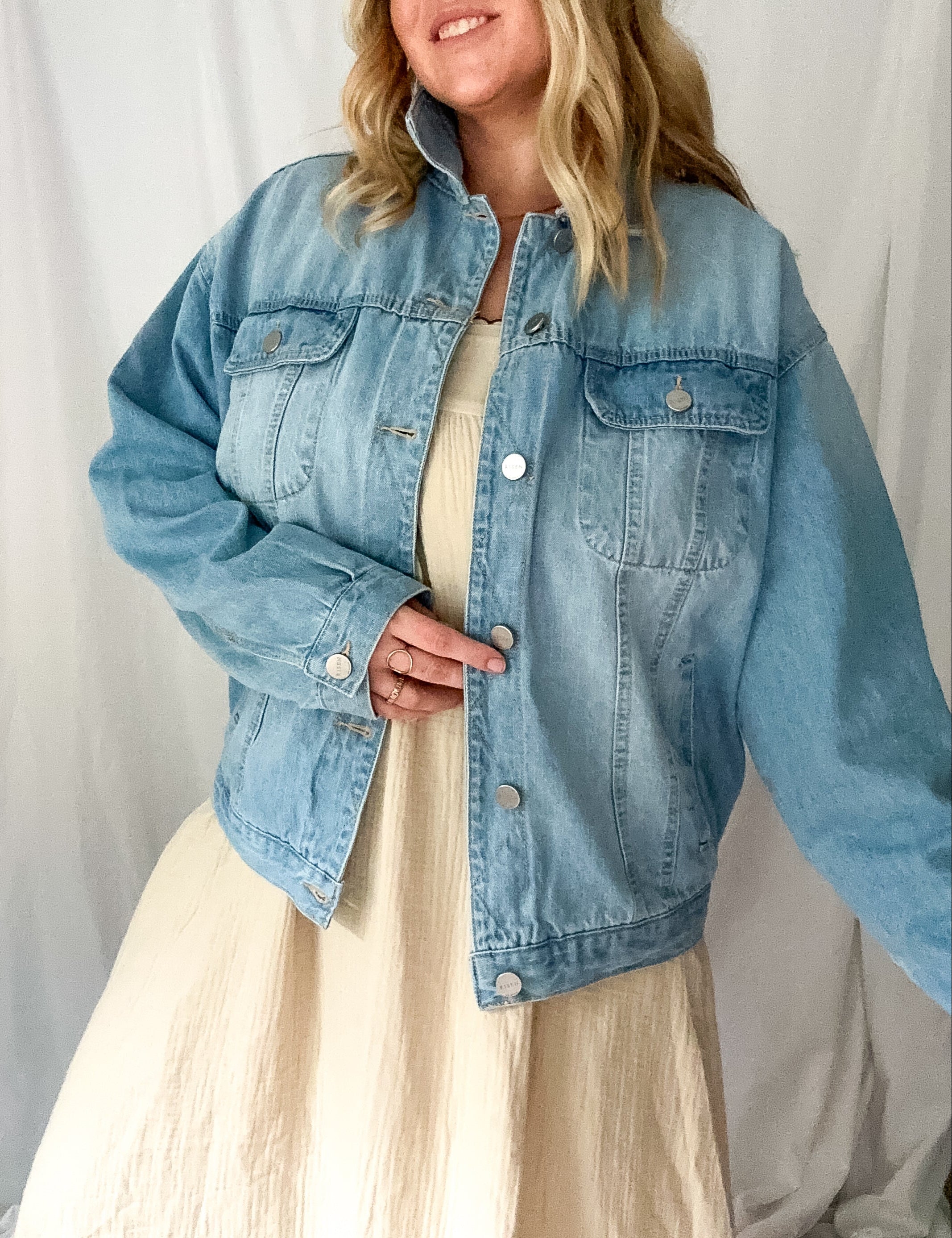 Woman wearing a light blue denim jacket over a beige dress against a white background