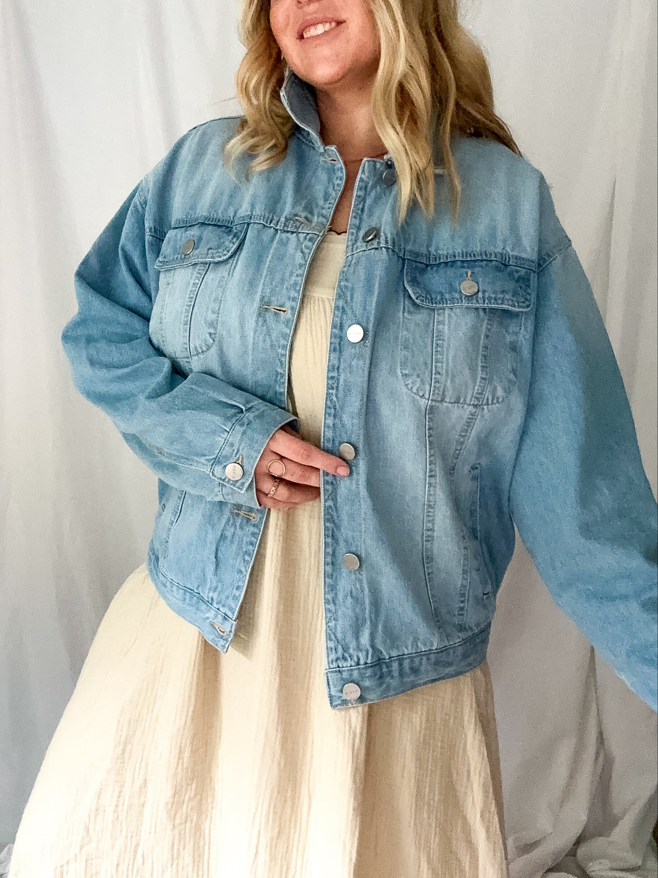 Woman wearing a light blue denim jacket over a beige dress against a white background