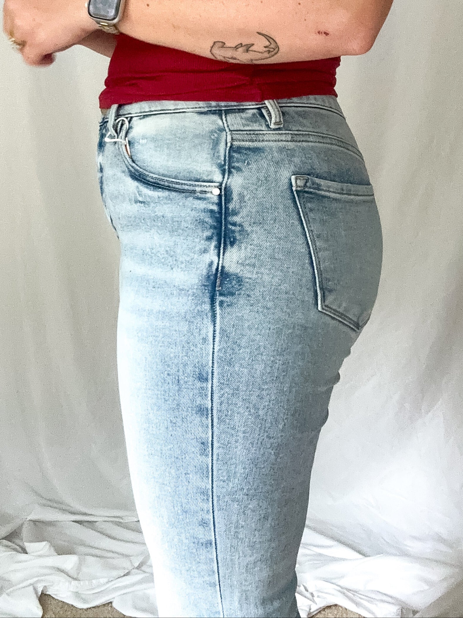 Person wearing a red tank top and light blue jeans against a plain background