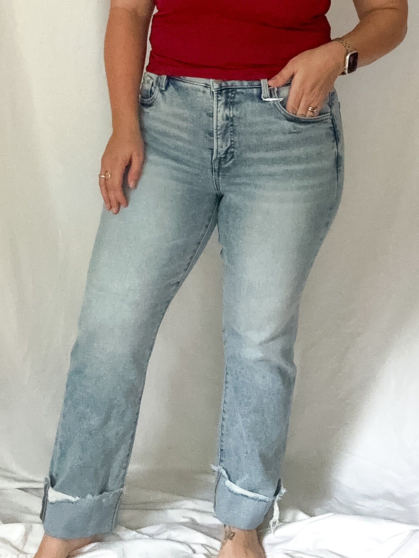 Woman wearing a red top and light blue jeans against a white curtain background