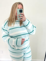 Person wearing a light blue and white striped sweater and pants set, taking a mirror selfie.