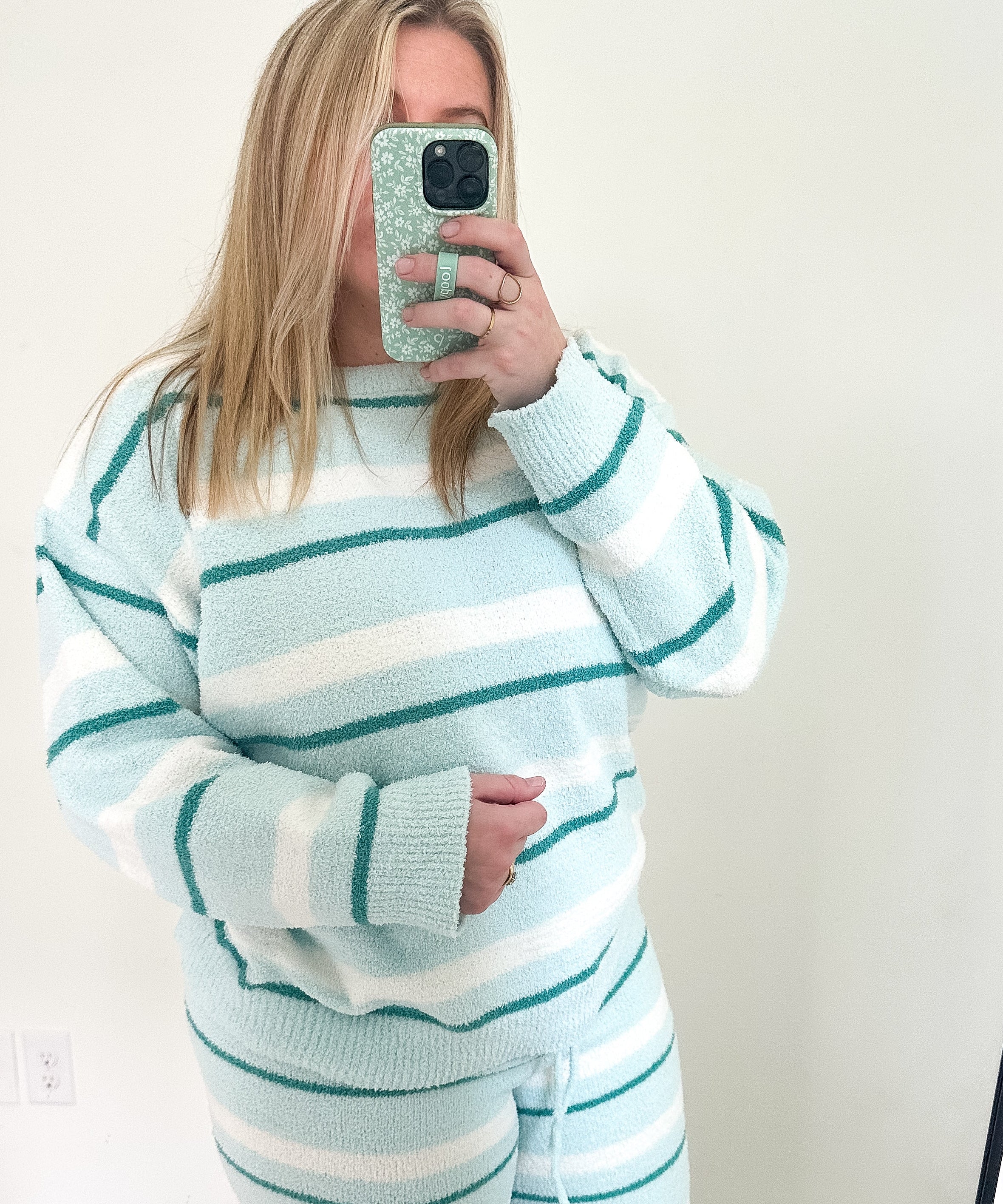 Person wearing a light blue and white striped sweater and pants set, taking a mirror selfie.