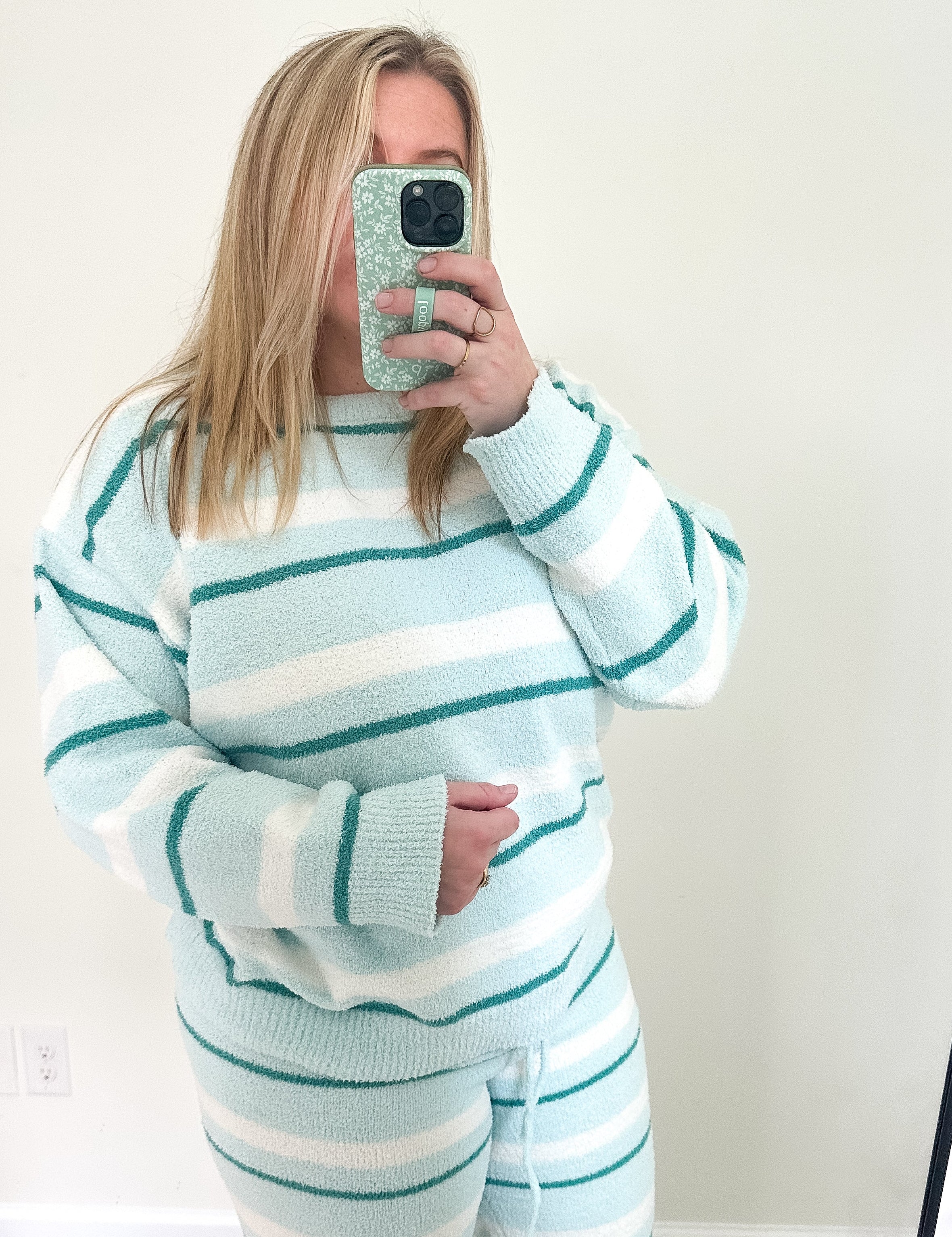 Person wearing a light blue and white striped sweater and pants set, taking a mirror selfie.