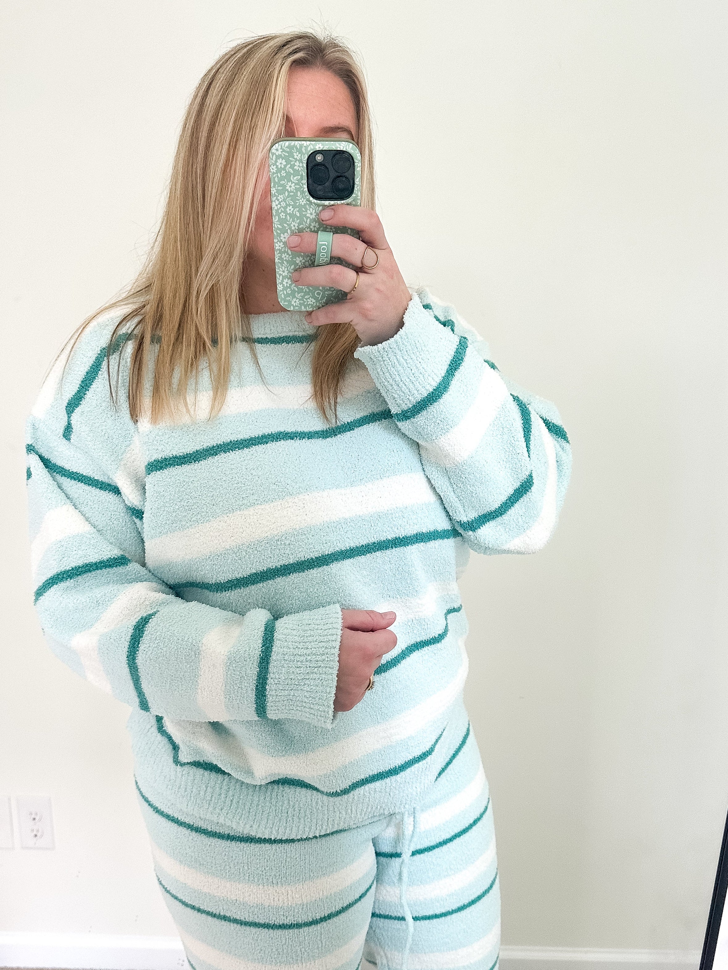 Person wearing a light blue and white striped sweater and pants set, taking a mirror selfie.