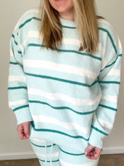 Person wearing a light blue and white striped sweater and pants indoors.