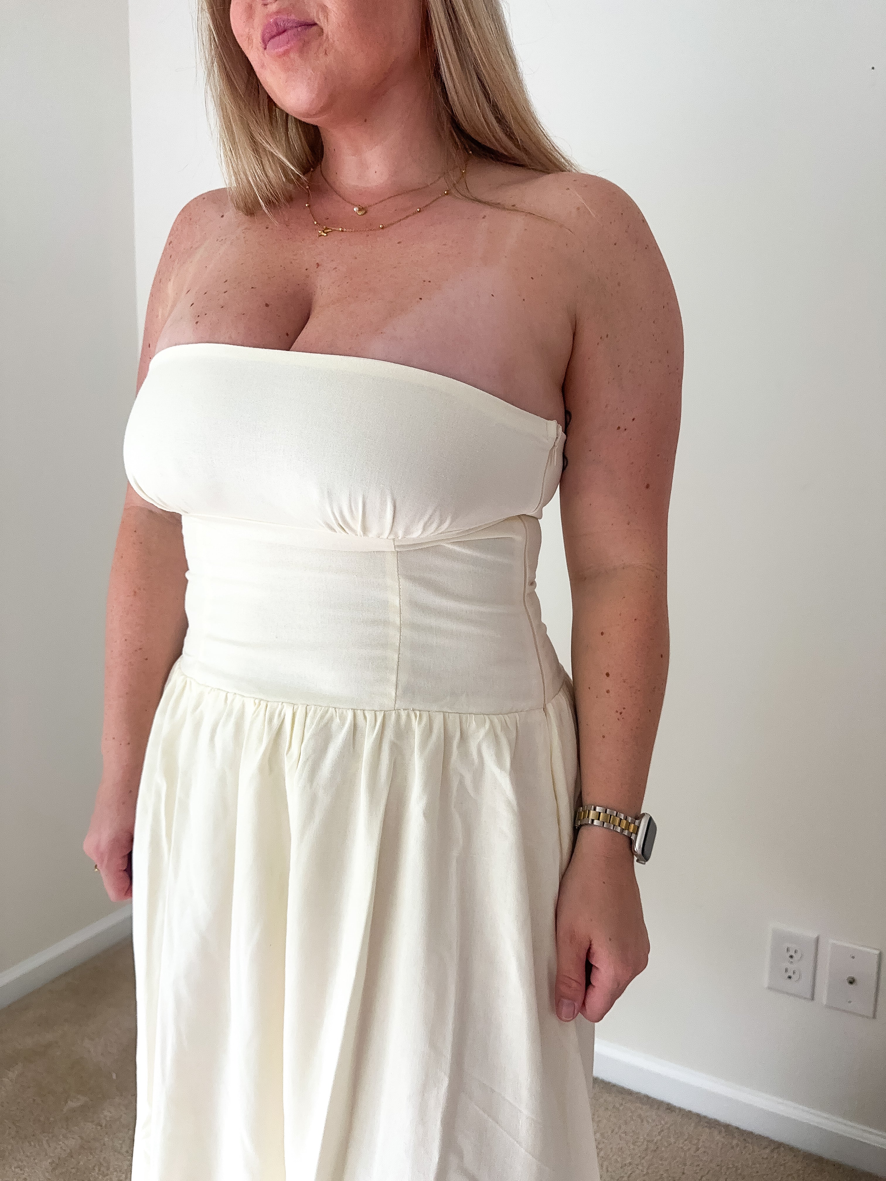 Woman wearing a strapless white dress indoors against a plain wall.