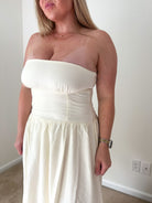 Woman wearing a strapless white dress indoors against a plain wall.
