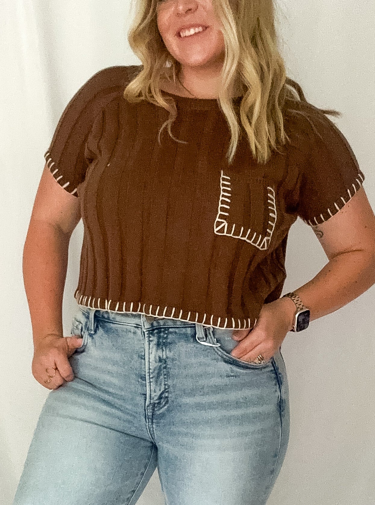 Woman wearing a brown top with fringe details and light blue jeans against a white background