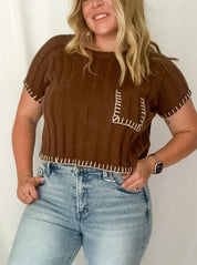 Woman wearing a brown top with fringe details and light blue jeans against a white background