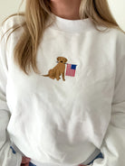 White sweatshirt with a dog holding an American flag patch worn by a person.