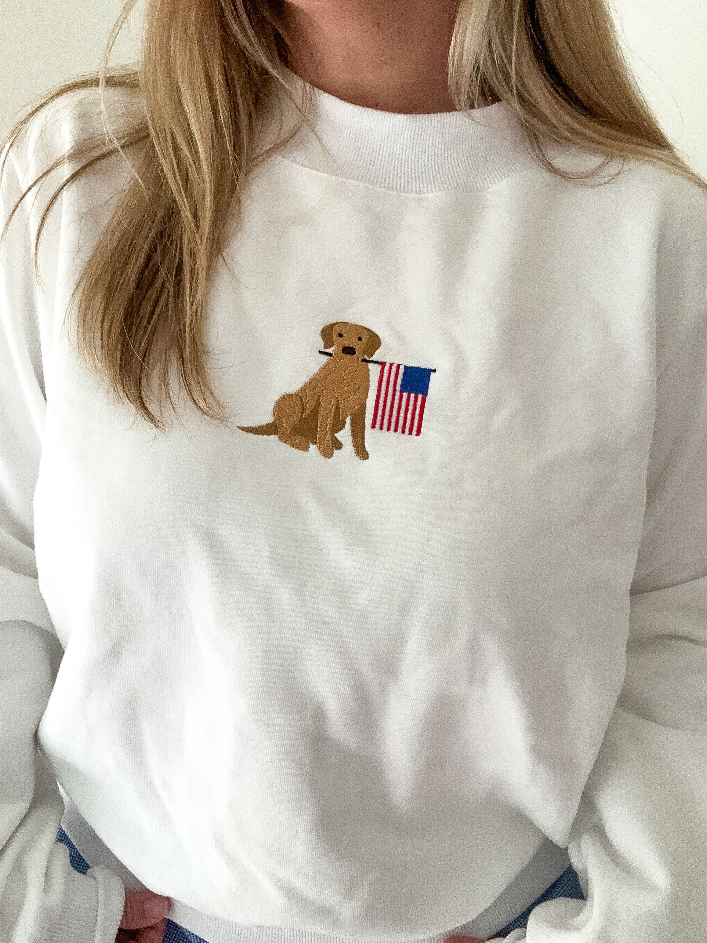 White sweatshirt with a dog holding an American flag patch worn by a person.