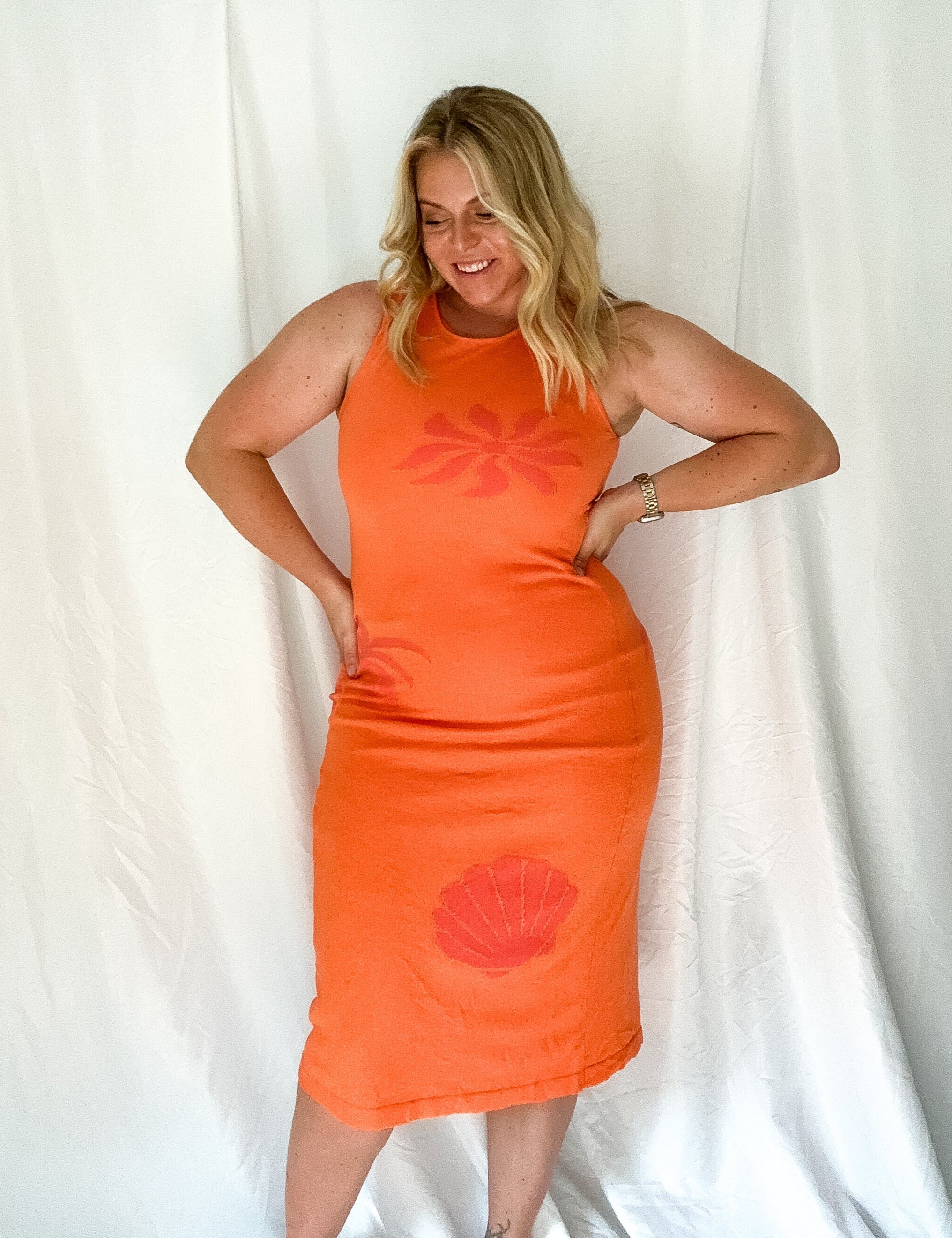 Woman wearing an orange dress with a red floral design against a white background