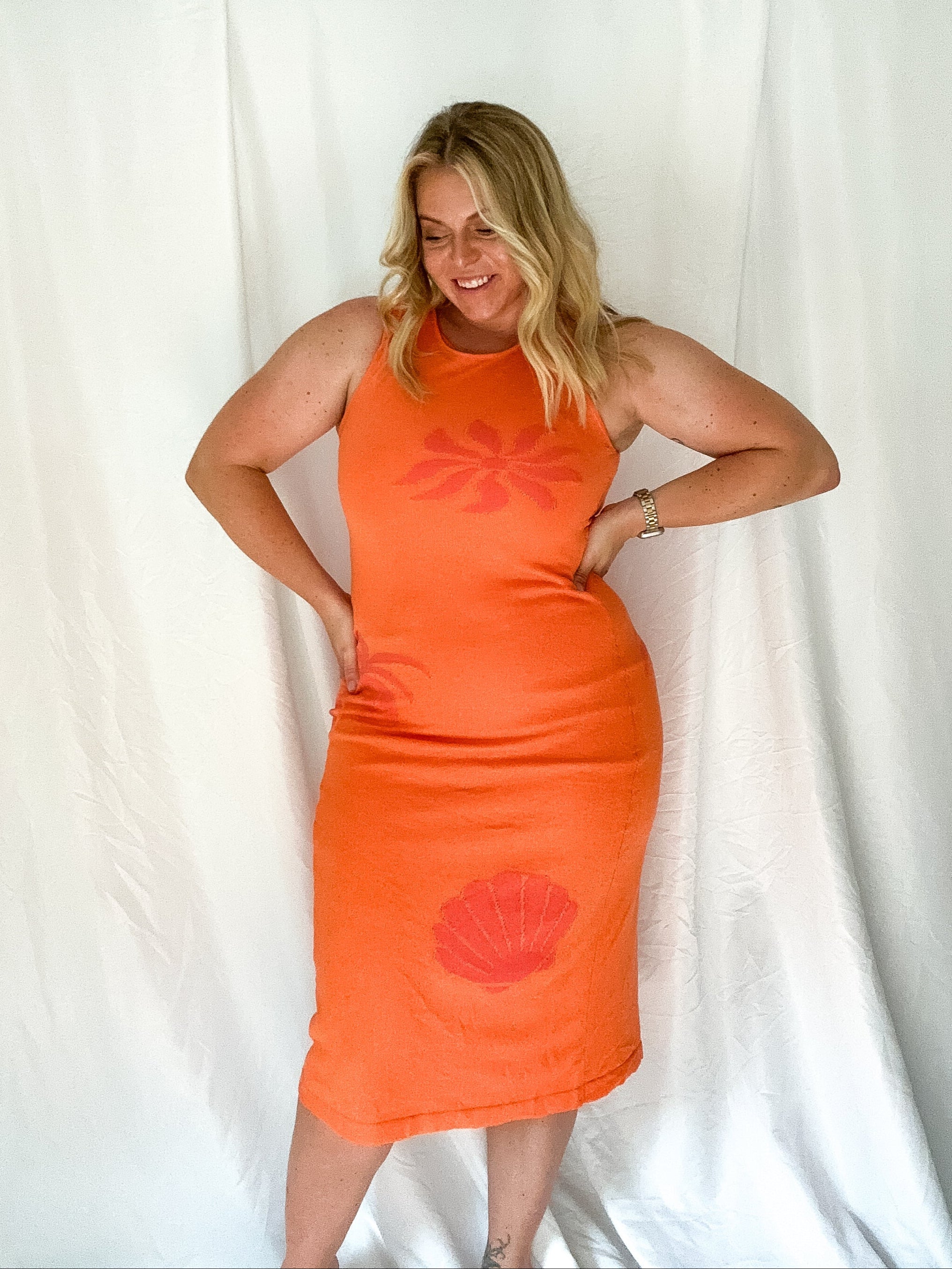 Woman wearing an orange dress with a red floral design against a white background