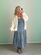 A woman wearing a cream-colored oversized sweater cardigan over a checkered dress.