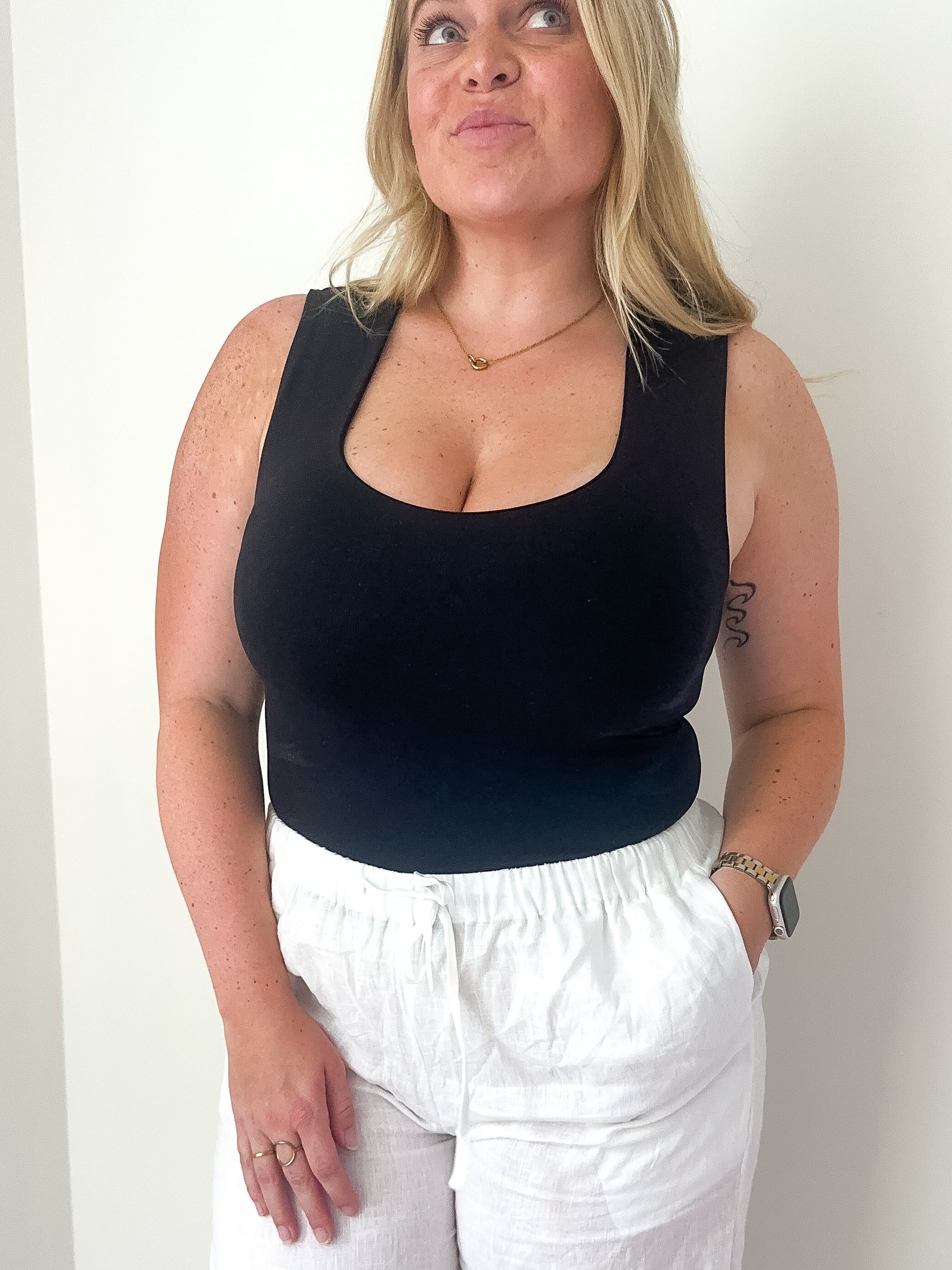 A woman wearing a black sleeveless crop tank with white pants, showcasing a fitted silhouette.
