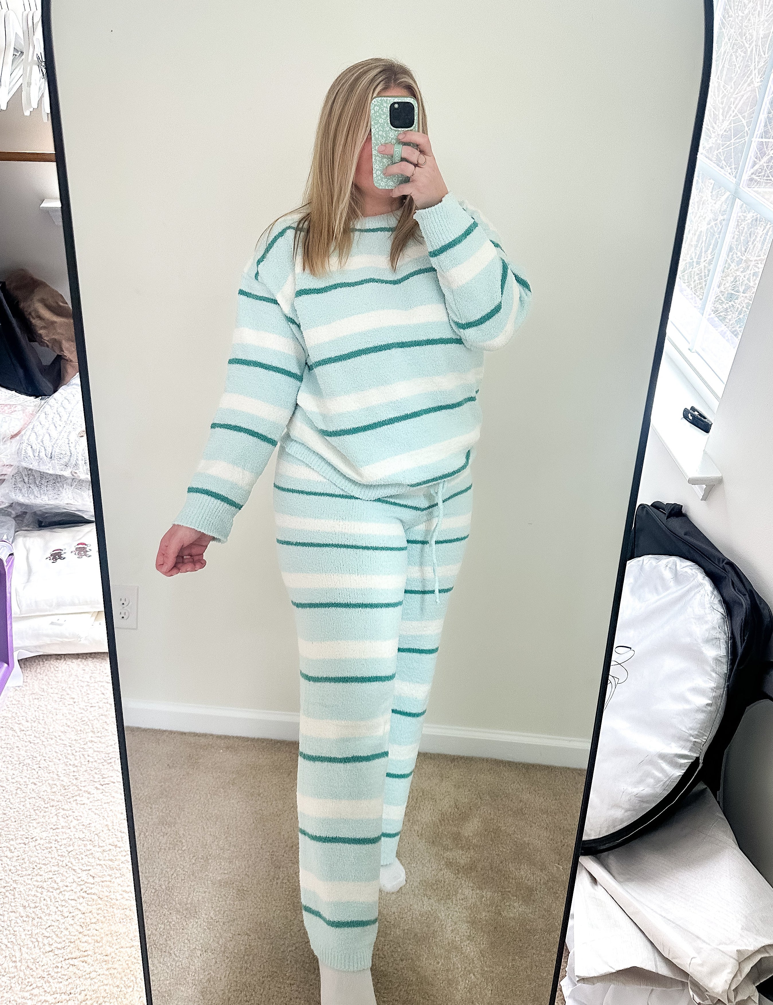 Person wearing a light blue and white striped pajama set taking a mirror selfie.
