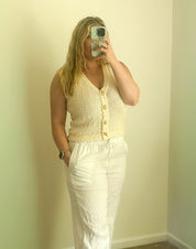 Person taking a mirror selfie wearing a yellow sleeveless top and white pants in a room with light green walls.