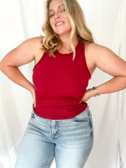 Woman wearing a red tank top and light blue jeans against a white background