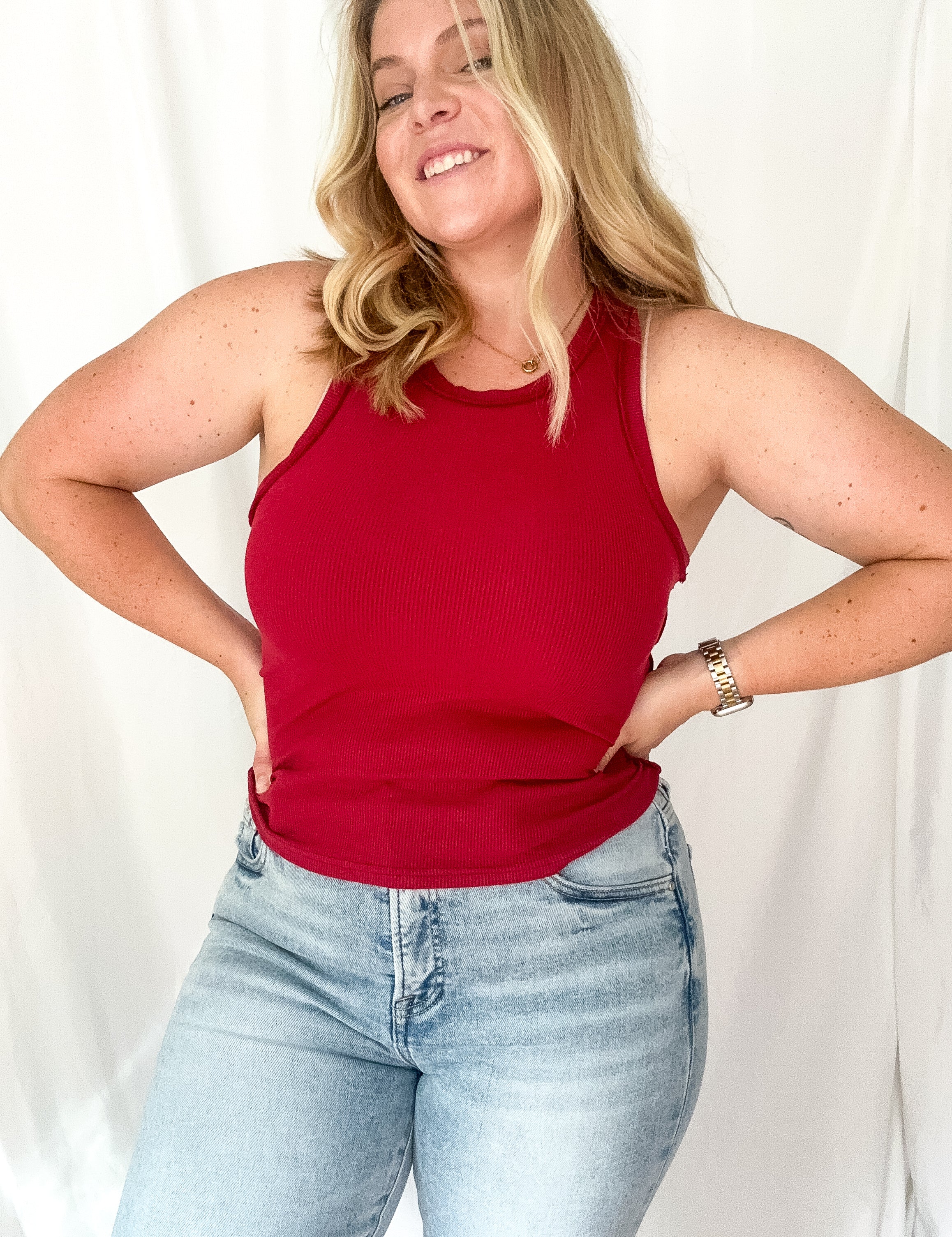 Woman wearing a red tank top and light blue jeans against a white background