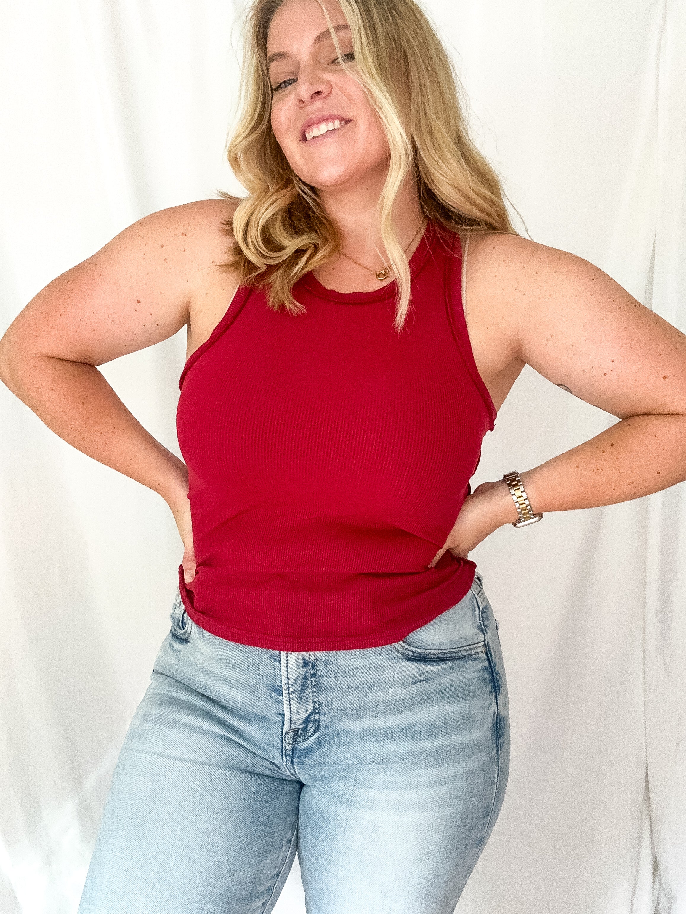 Woman wearing a red tank top and light blue jeans against a white background