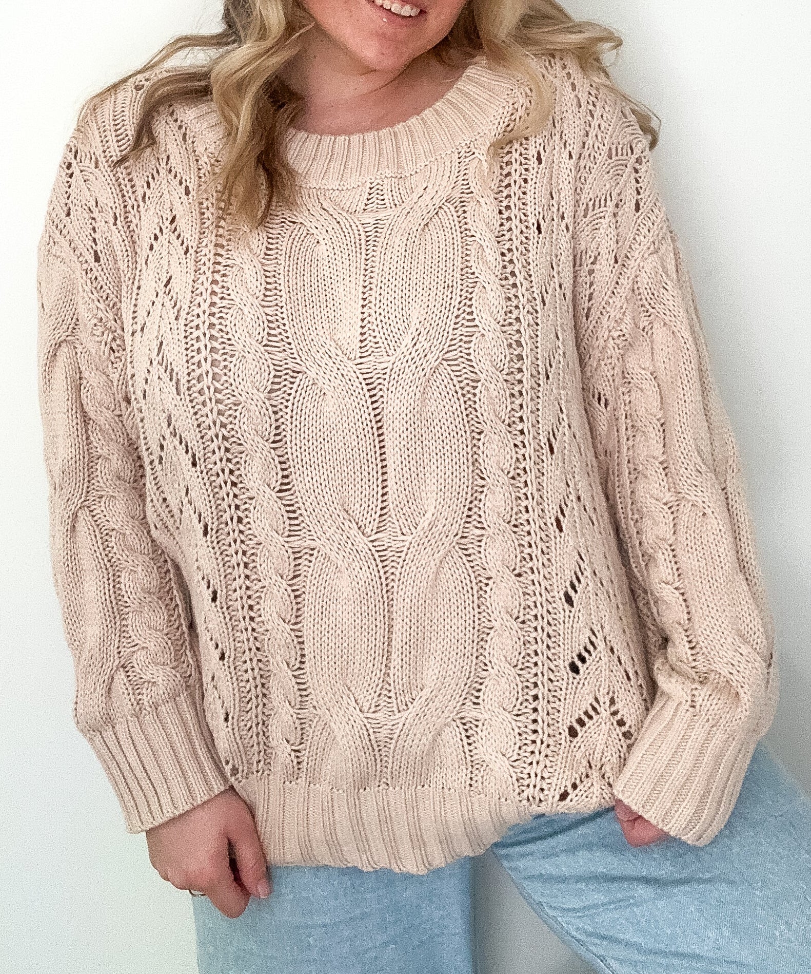 Woman wearing a beige cable knit sweater against a white background