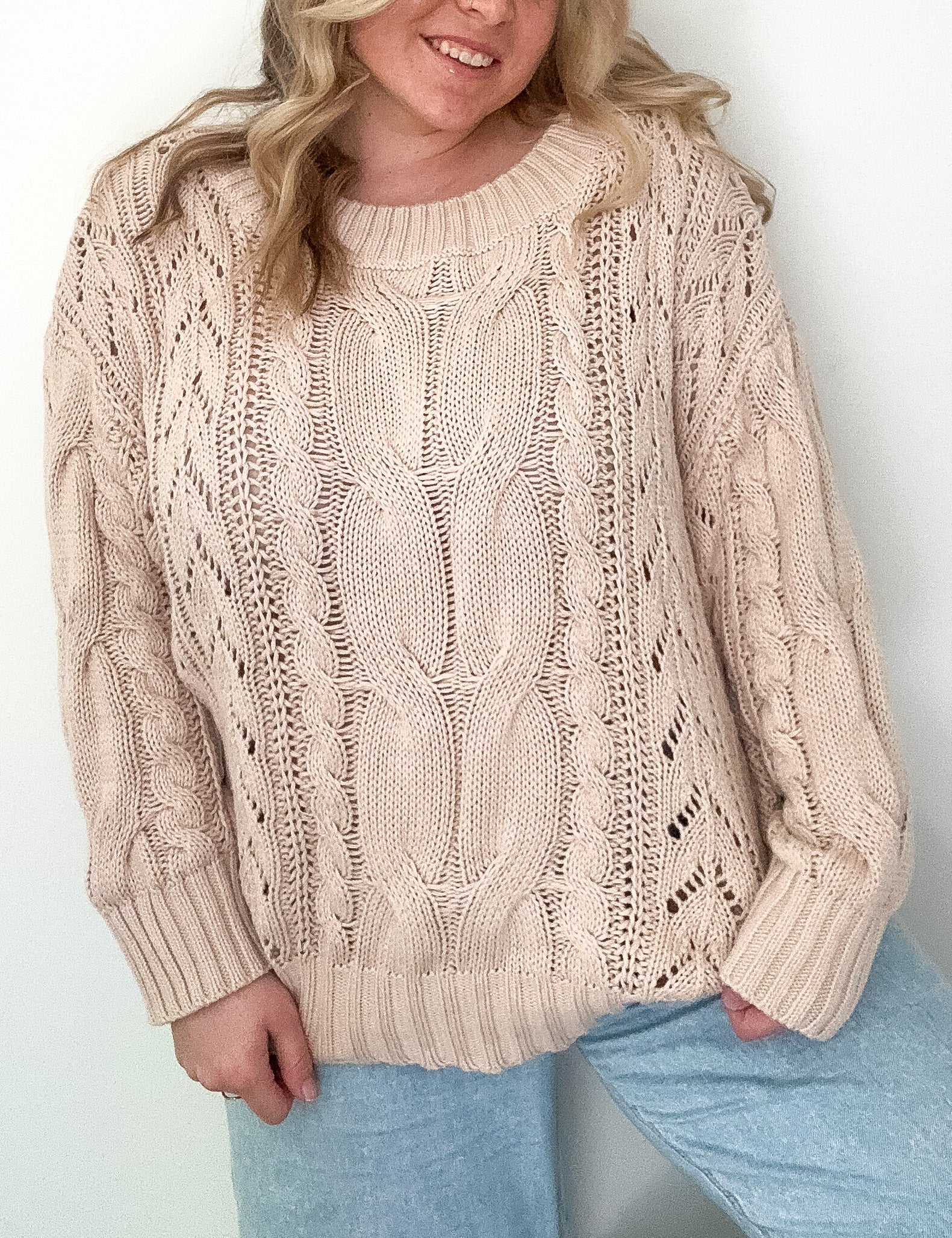 Woman wearing a beige cable knit sweater against a white background