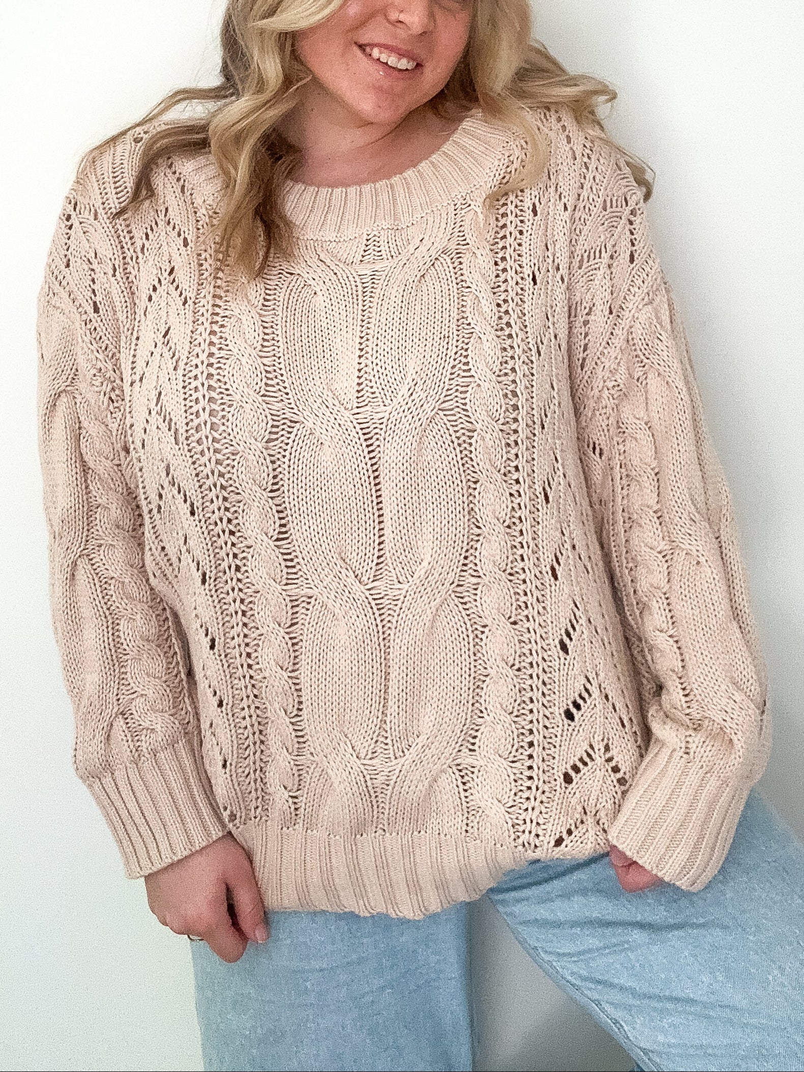 Woman wearing a beige cable knit sweater against a white background