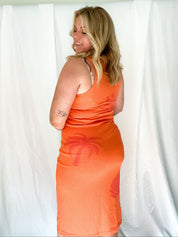 Woman wearing an orange dress with palm tree design against a white background