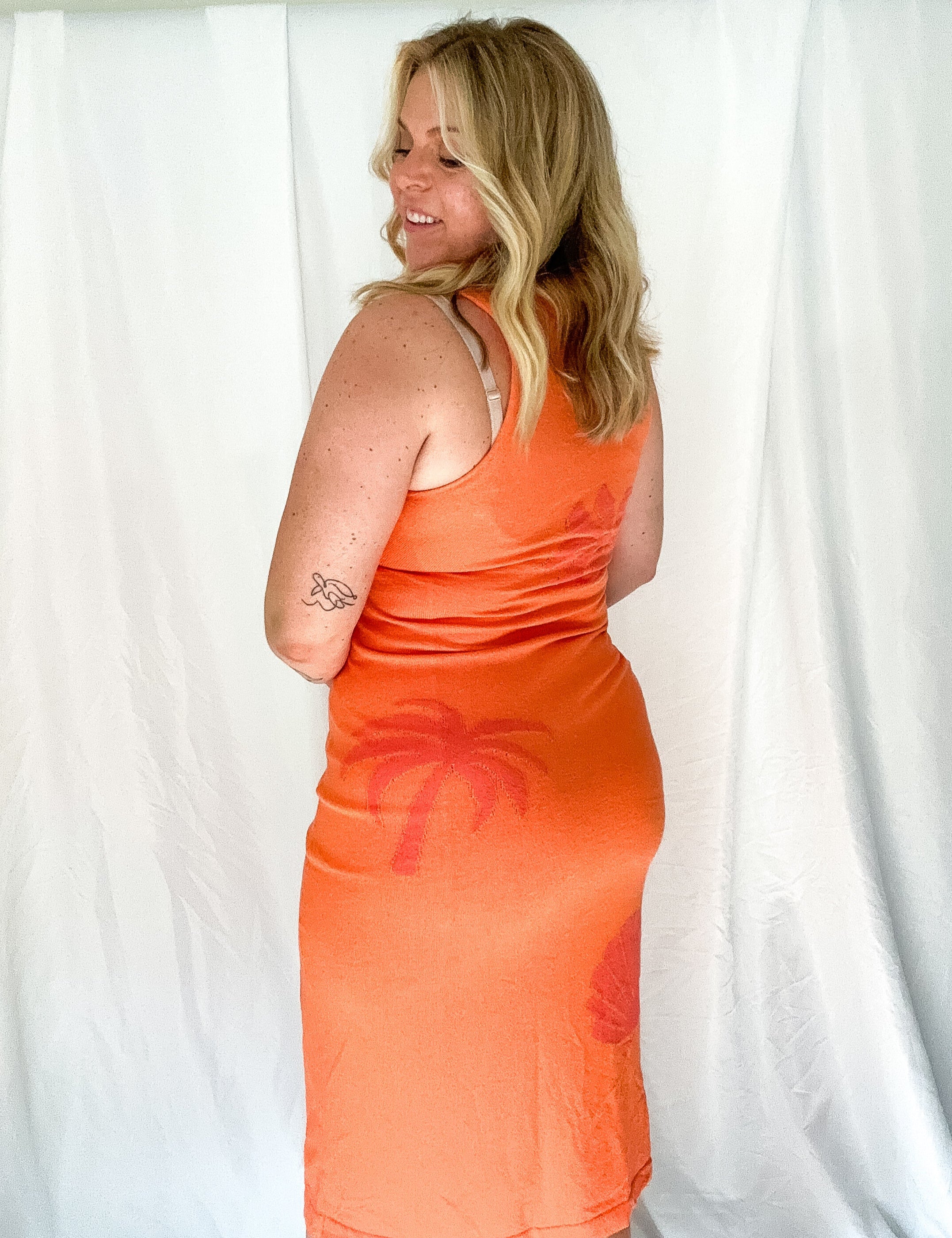 Woman wearing an orange dress with palm tree design against a white background