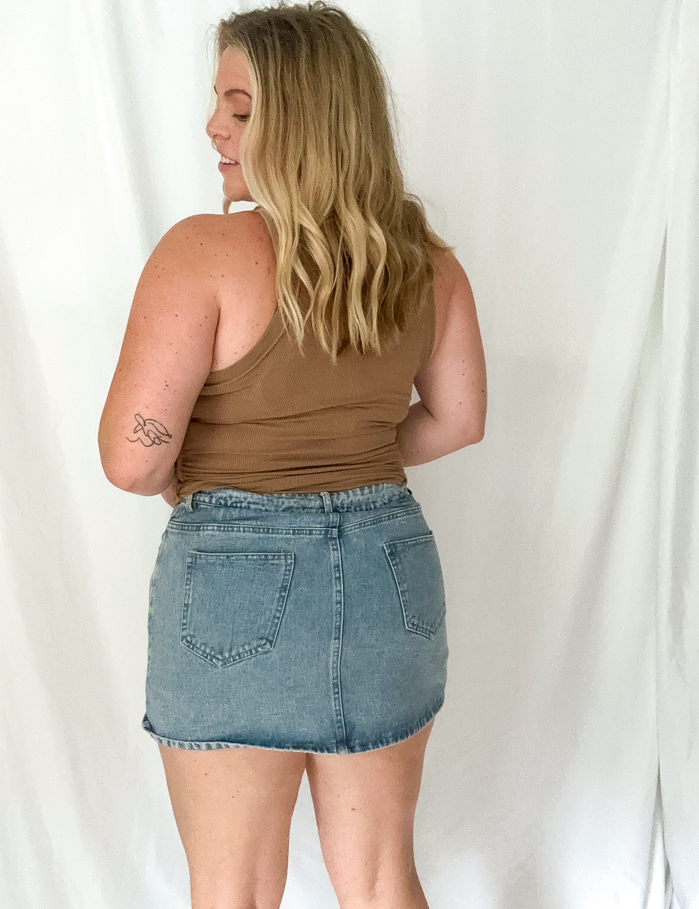 Woman wearing a brown tank top and denim skirt against a white background