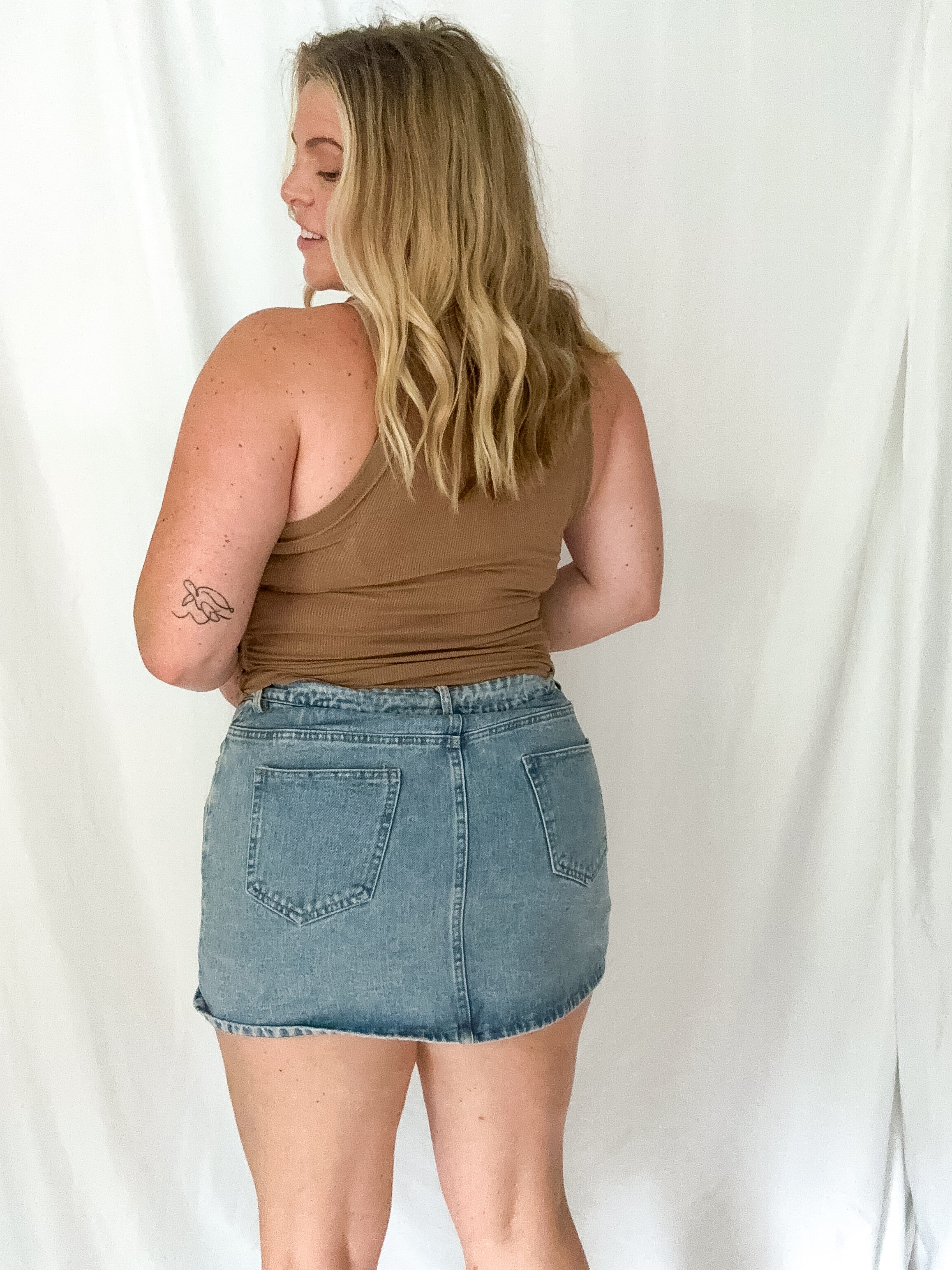 Woman wearing a brown tank top and denim skirt against a white background